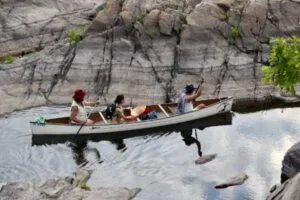 Three paddlers in a canoe by rock face