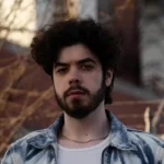 Man with dark beard outside in fall with a jean jacket