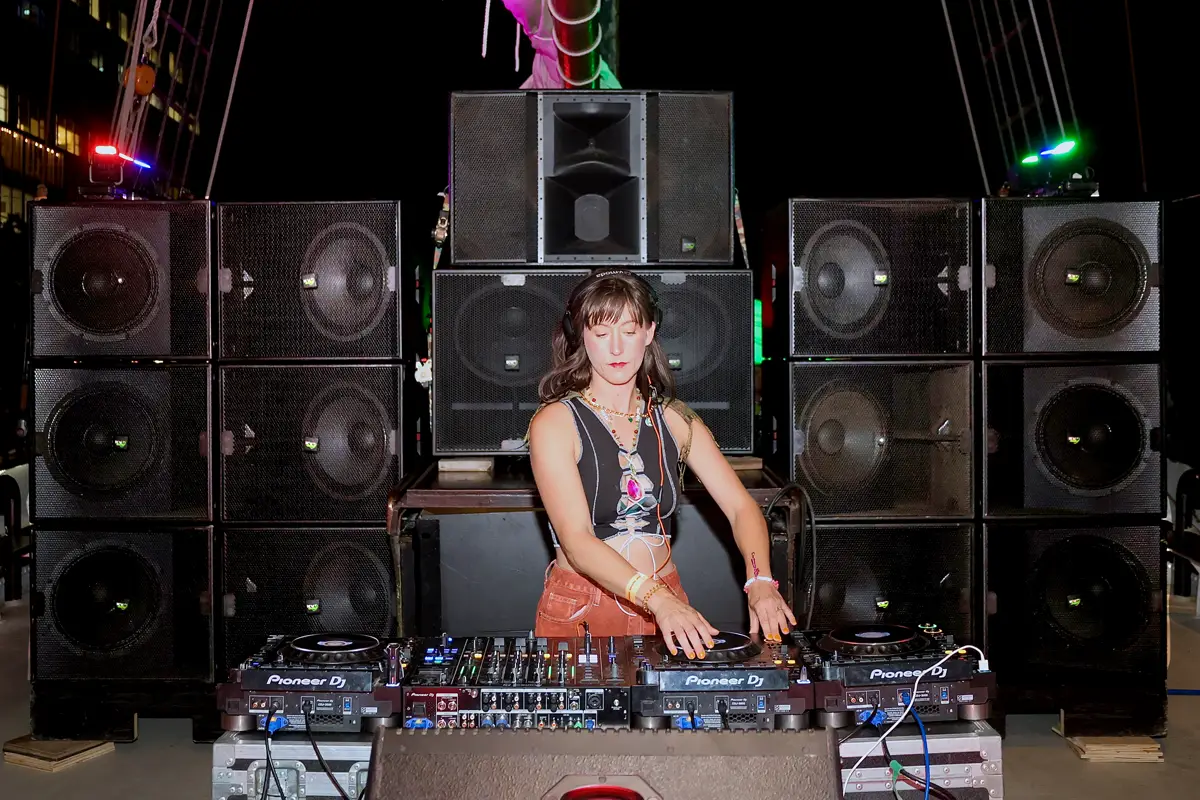 DJ with a large wall of bass bins behind her on a tall ship