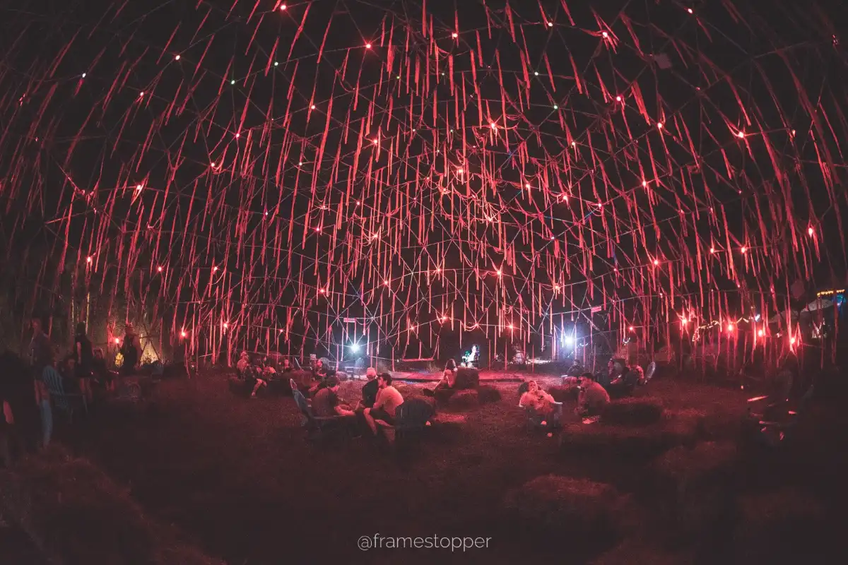 People resting looking up at streamers lit by red lights in a geodesic spaceship frame