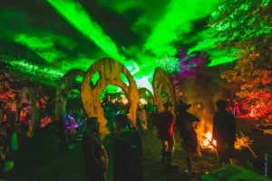 Green lasers on clouds over large circular sculptures of eyes with large round mouths and people talking around