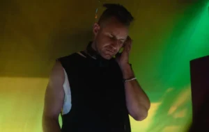 A man DJing with a green and yellow wall behind
