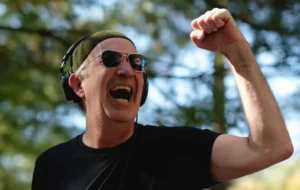 A man with his fist up, sunglasses, and a small green hat