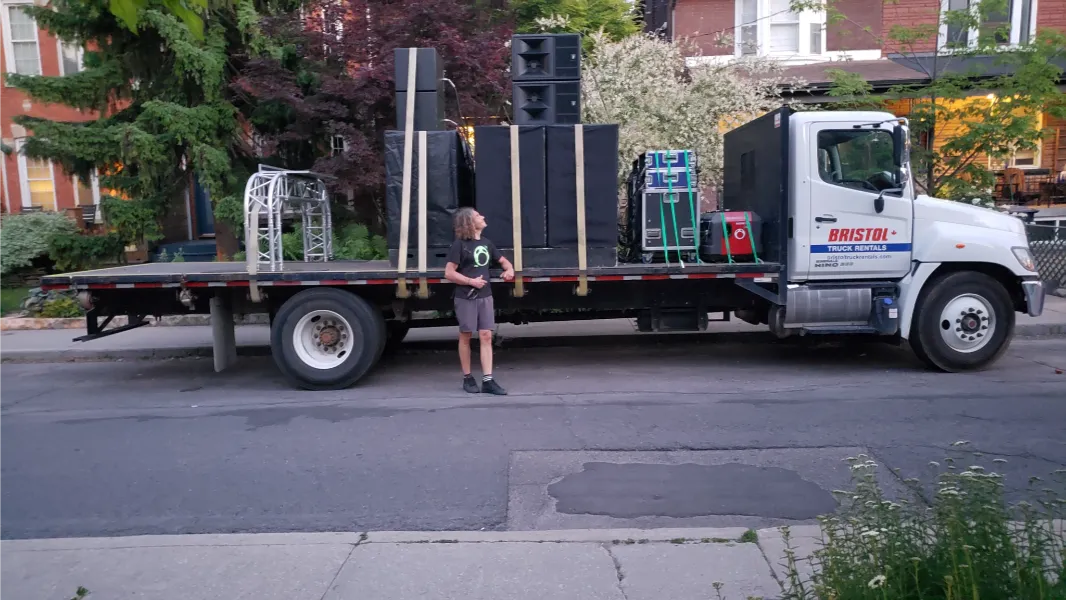 A long truck holding strapped down speakers and stage stand and a crew member