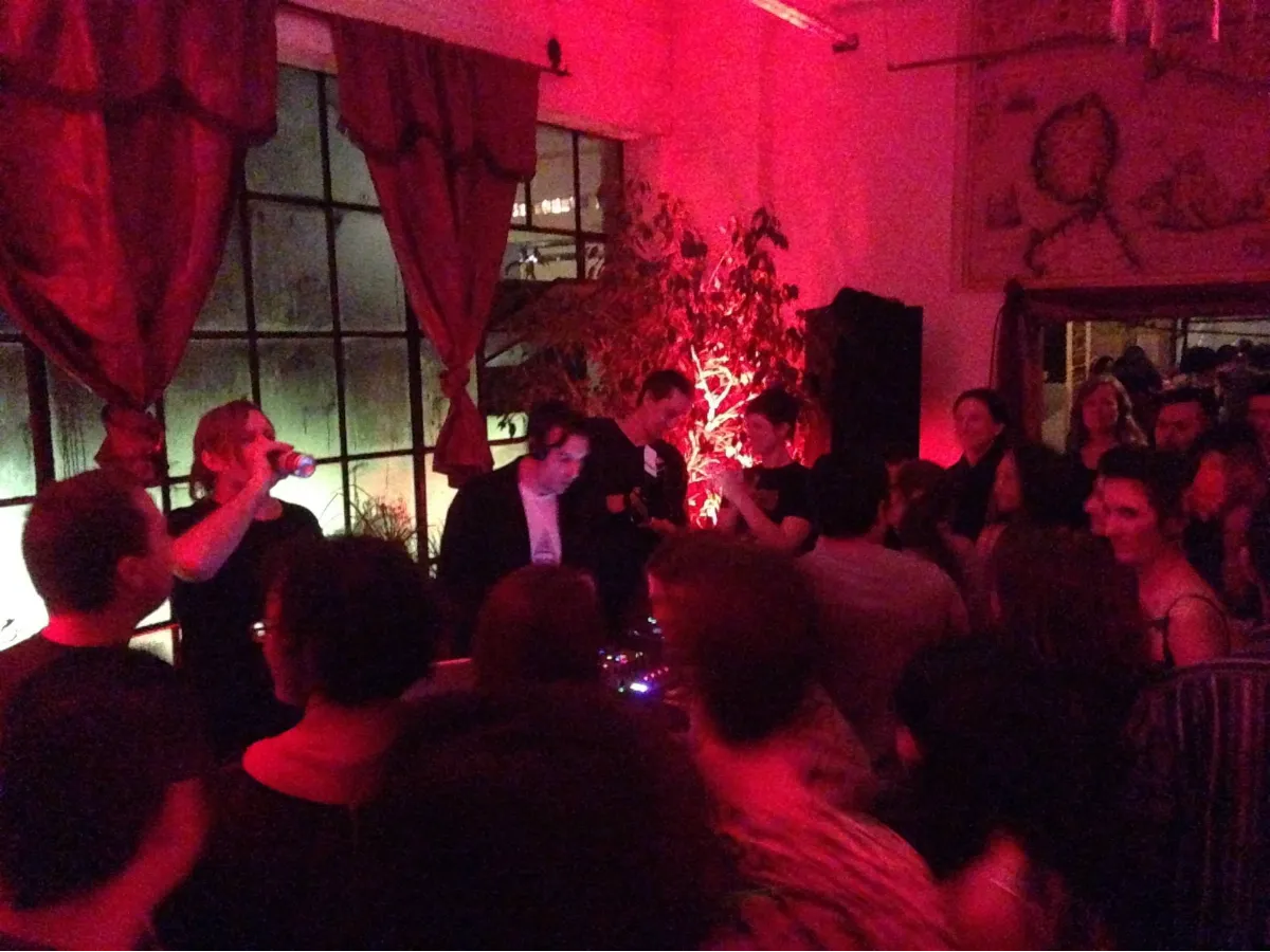Two DJs in a crowded red lit room of dancers