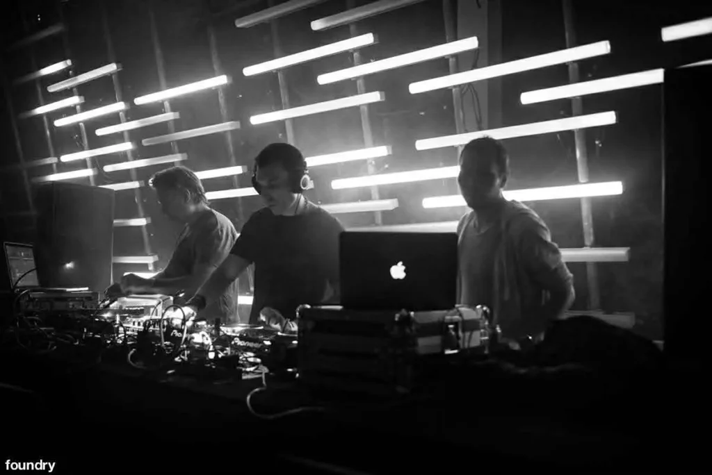 Three DJs by wall with white horizontal lights