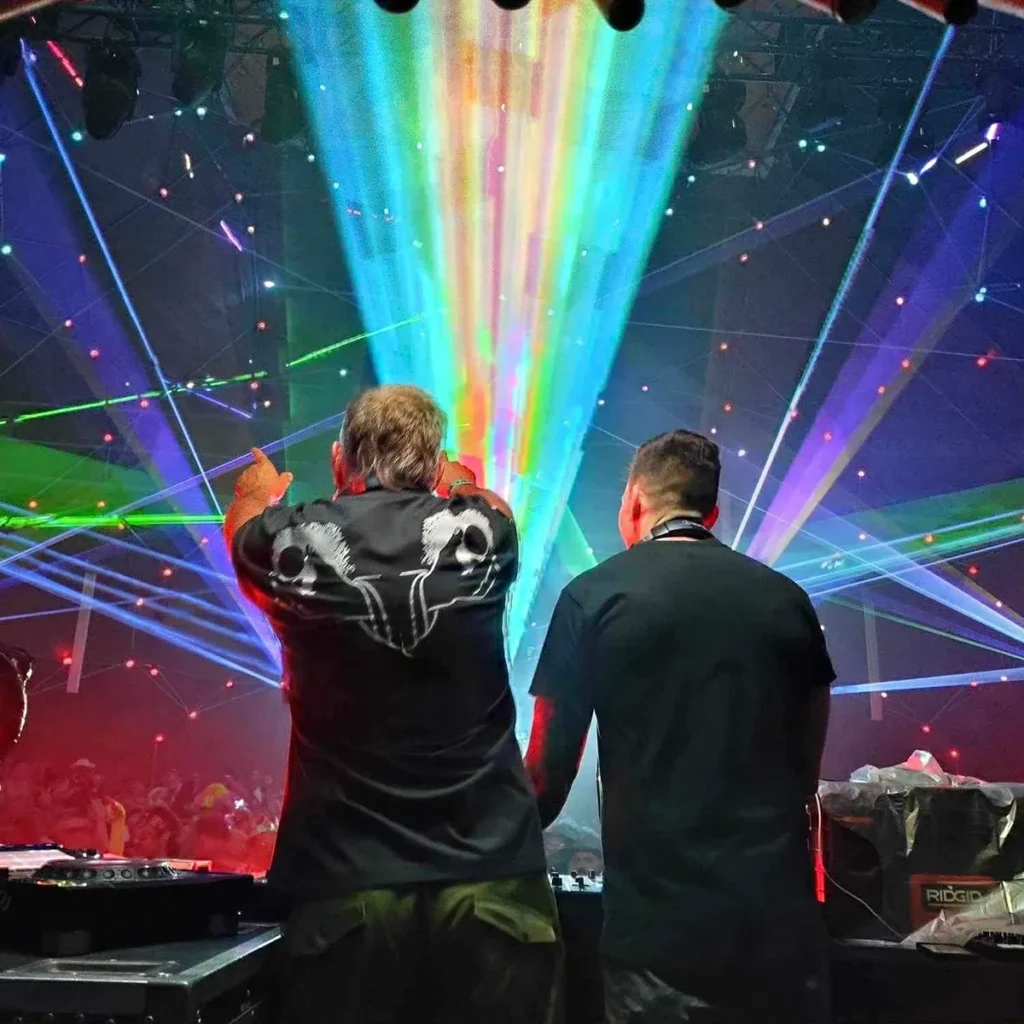 Two DJs with colourful lasers and crowd beyond 