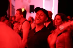 Man in black cap and shirt laughing at a red-lit party
