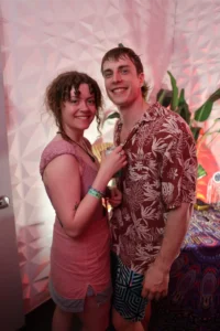 Couple smiling at a festival, woman in pink dress, man in Hawaiian shirt