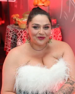 Plus-size woman in white feather top and hoop earrings smiles at the camera.