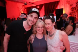 Three smiling friends at a vibrant party with red lighting and disco ball
