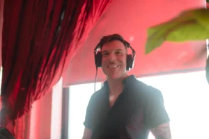 Smiling DJ wearing headphones, performing at a vibrant event with red drapes