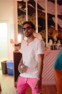 Man in white t-shirt and pink shorts holding a drink with sunglasses