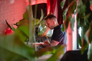 DJ with tattoos mixing music at a party with lush green plants