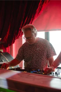 DJ with gray hair wearing a leopard print shirt plays music on a DJ setup.