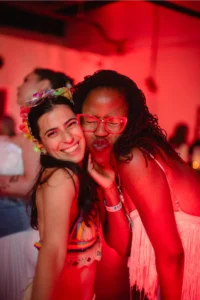 Two women smiling and posing for a photo at a party, one with a flower crown