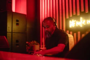 DJ in headphones plays music at a club with red lighting and neon sign