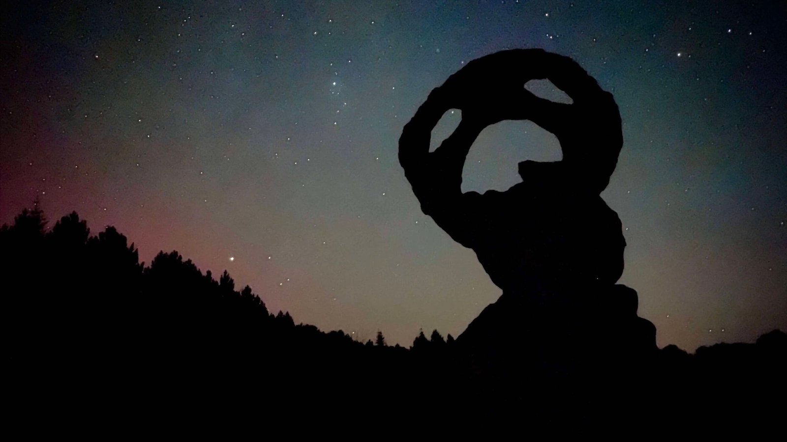 Silhouette of a balanced rock formation under a starry sky with faint aurora