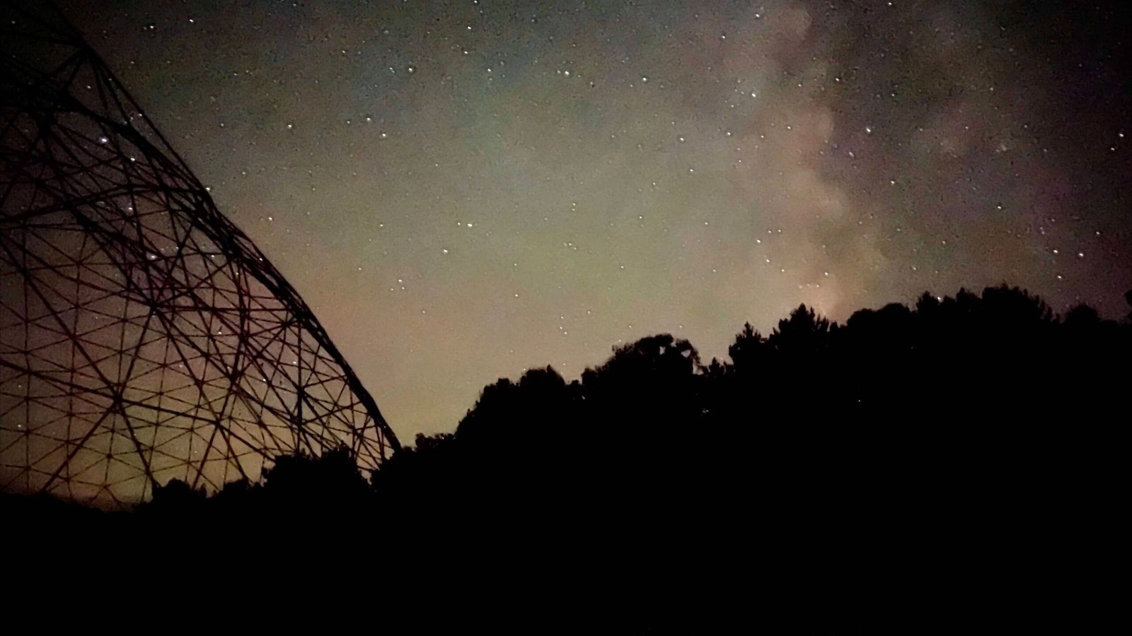 Silhouette of trees and a radio telescope tower under the Perseid meteor shower, hinting at Harvest 2026 ticket prices.